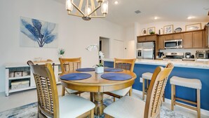 A modern kitchen with wooden cabinets, a central island, and a dining area with a round table and chairs. - Lanai & Resort Amenities: The Villages Getaway (Wildwood)