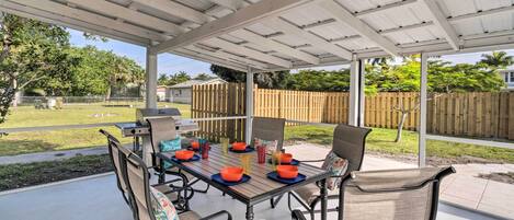 Une terrasse extérieure dotée d’une table et de chaises abritées, entourée d’une clôture en bois et de verdure.
