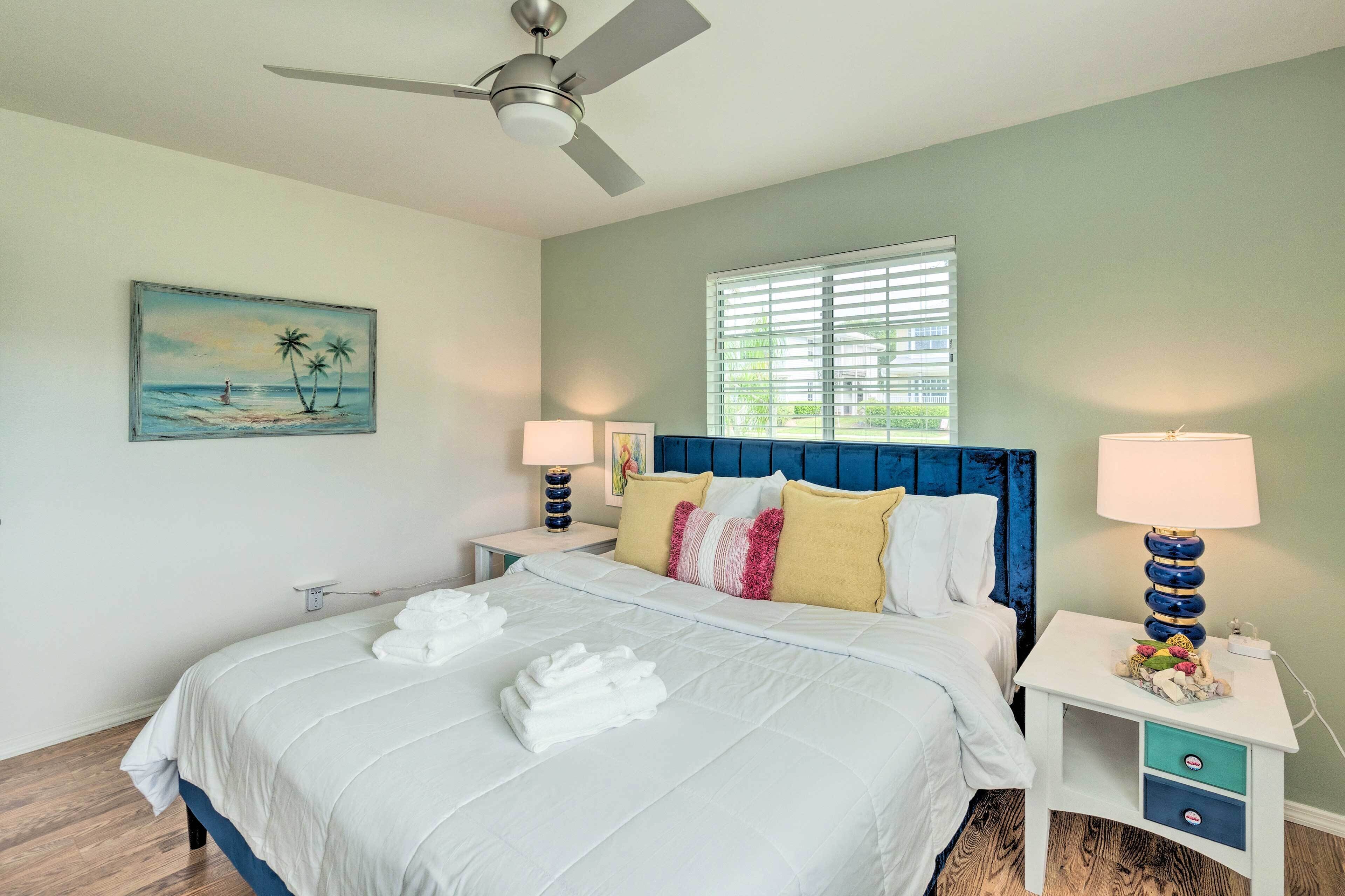 A neatly made bed with white linens and towels, a blue headboard, and a painting of a beach scene on the wall.