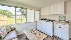 A compact kitchen with a built-in washer and dryer, a window with blinds, a wooden table with a candelabra, and a beige sofa with a decorative pillow. - Punta Gorda Retreat Near Historic Downtown! (Punta Gorda)
