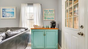 A living room with a teal cabinet, a grey sofa, and a beach-themed sign on the wall. - Pet-friendly PCB Duplex - Walk to Beach! (Panama City Beach)