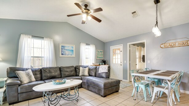 A living room with a sectional sofa, a dining table with chairs, a ceiling fan, and a sign that reads "BEACH HOUSE". - Pet-friendly PCB Duplex - Walk to Beach! (Panama City Beach)