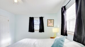 Een slaapkamer met een bed, een nachtkastje met een lamp, zwarte gordijnen en een raam met zonwering.