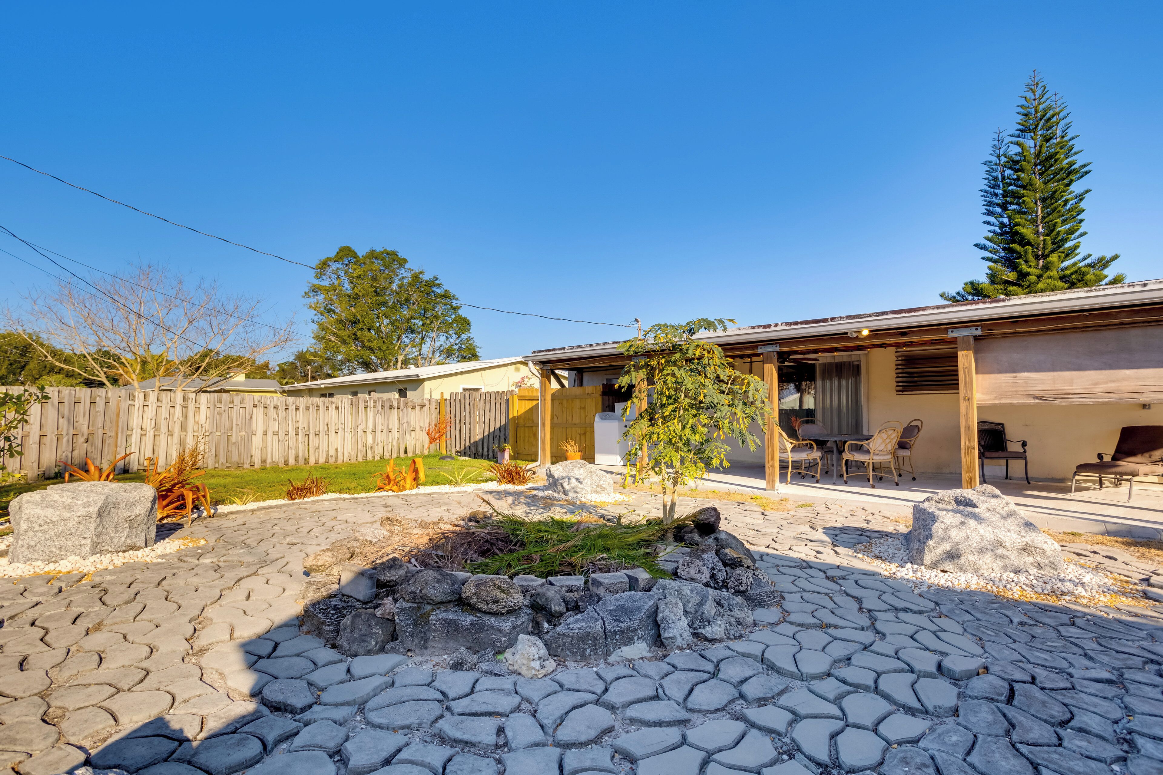 Una propiedad residencial con entrada pavimentada, cerca de madera, un pequeño jardín y un patio con mobiliario exterior.
