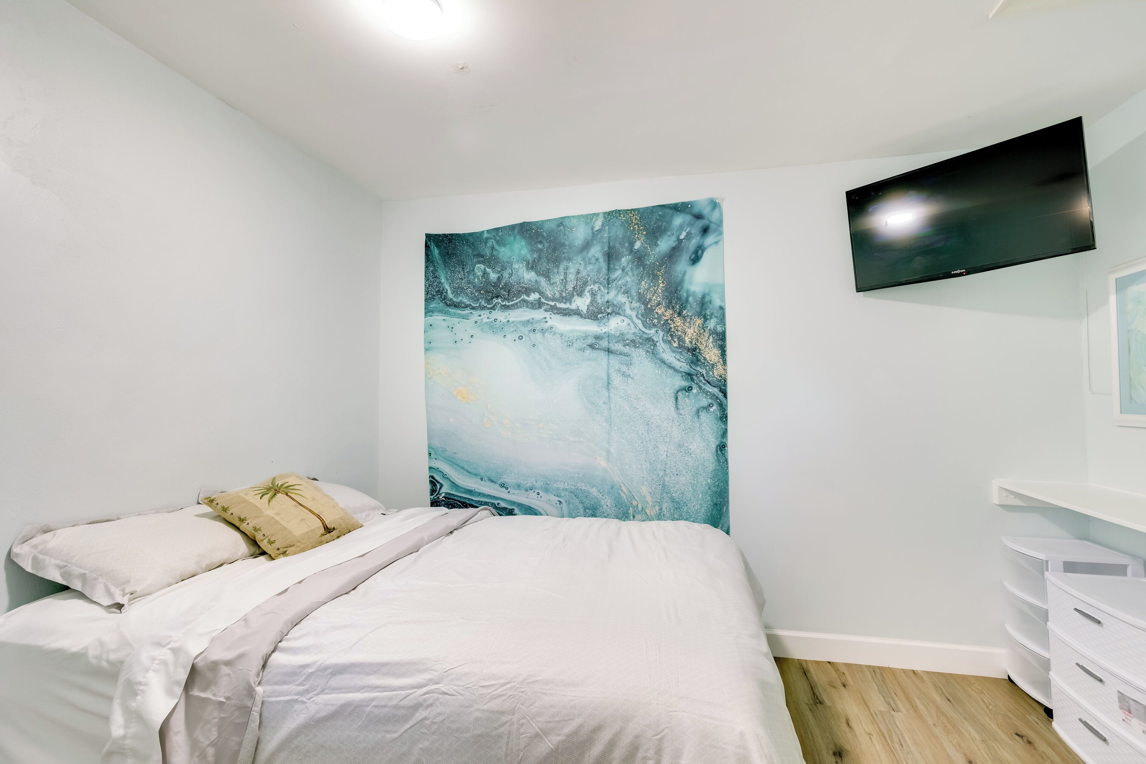 Un dormitorio con cama, un televisor montado en la pared y un cuadro abstracto grande.