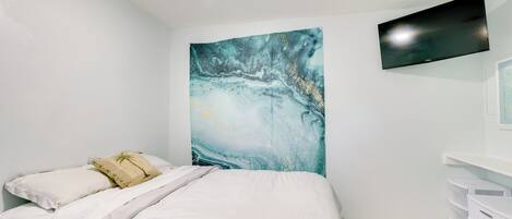 Un dormitorio con cama, un televisor montado en la pared y un cuadro abstracto grande.