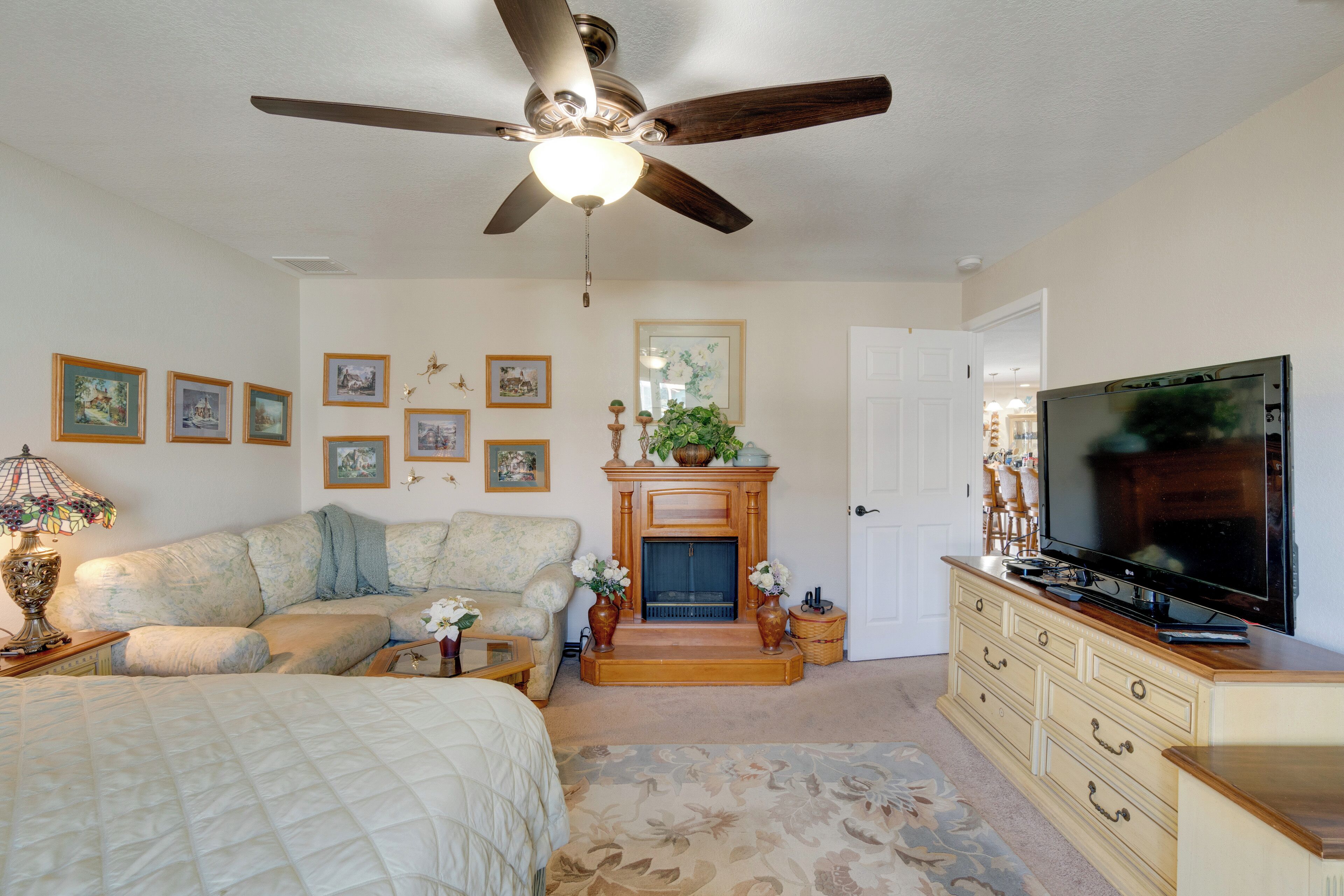 A bedroom with a bed, a sofa, a television, a fireplace, and a ceiling fan.