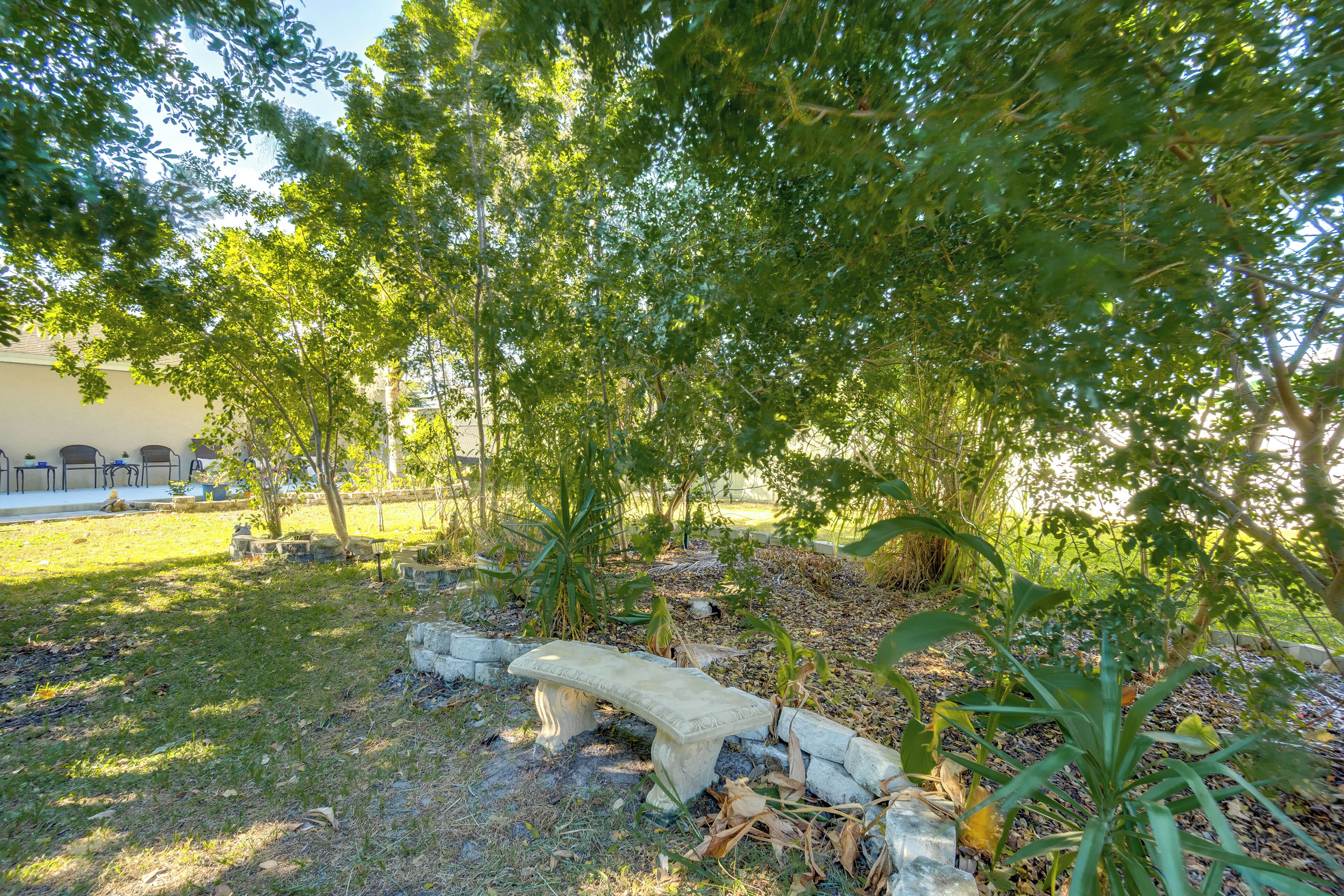 A stone bench in a garden with trees and a building in the background.