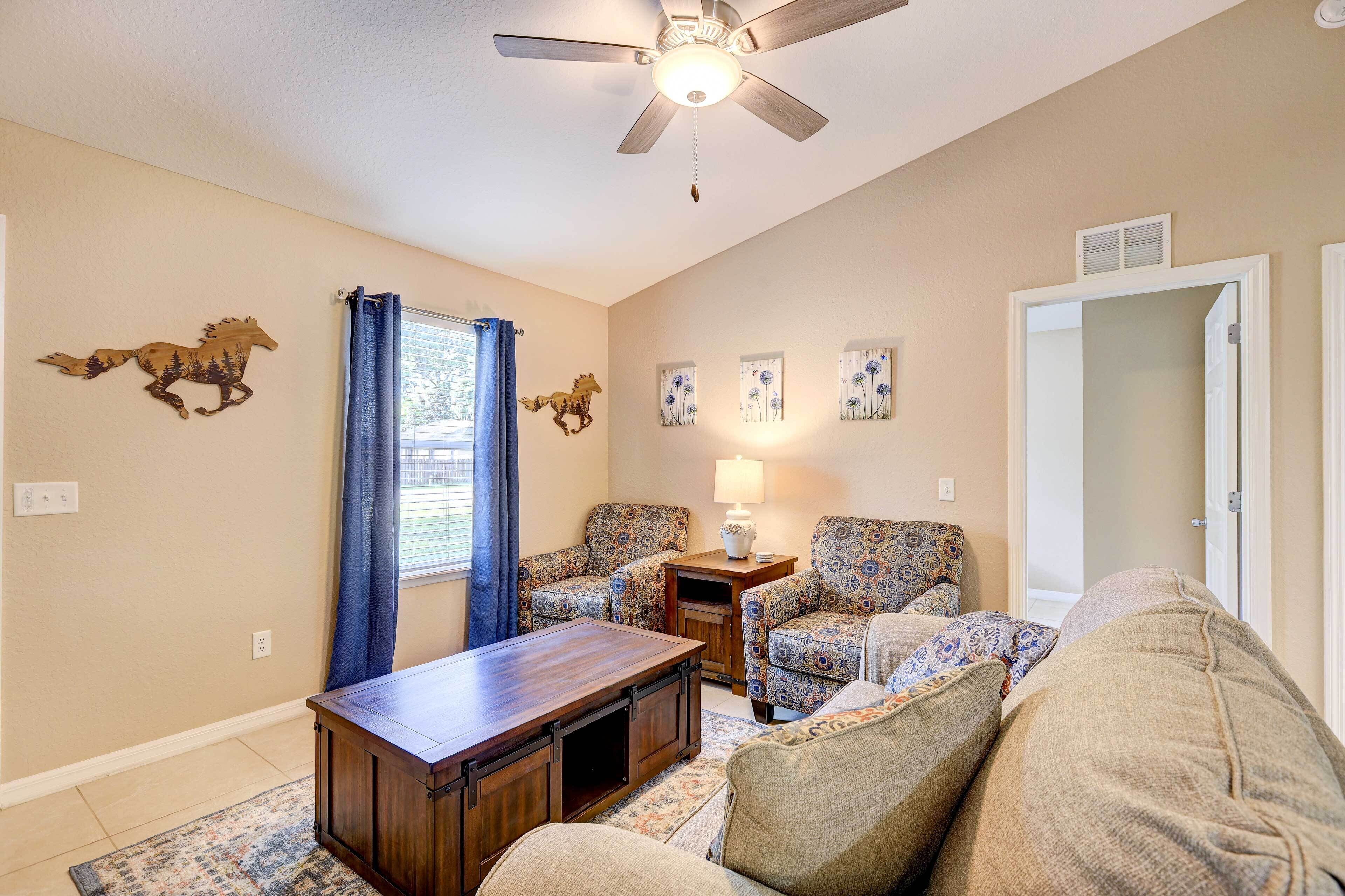 A living room with a ceiling fan, patterned chairs, a wooden coffee table, and wall art.
