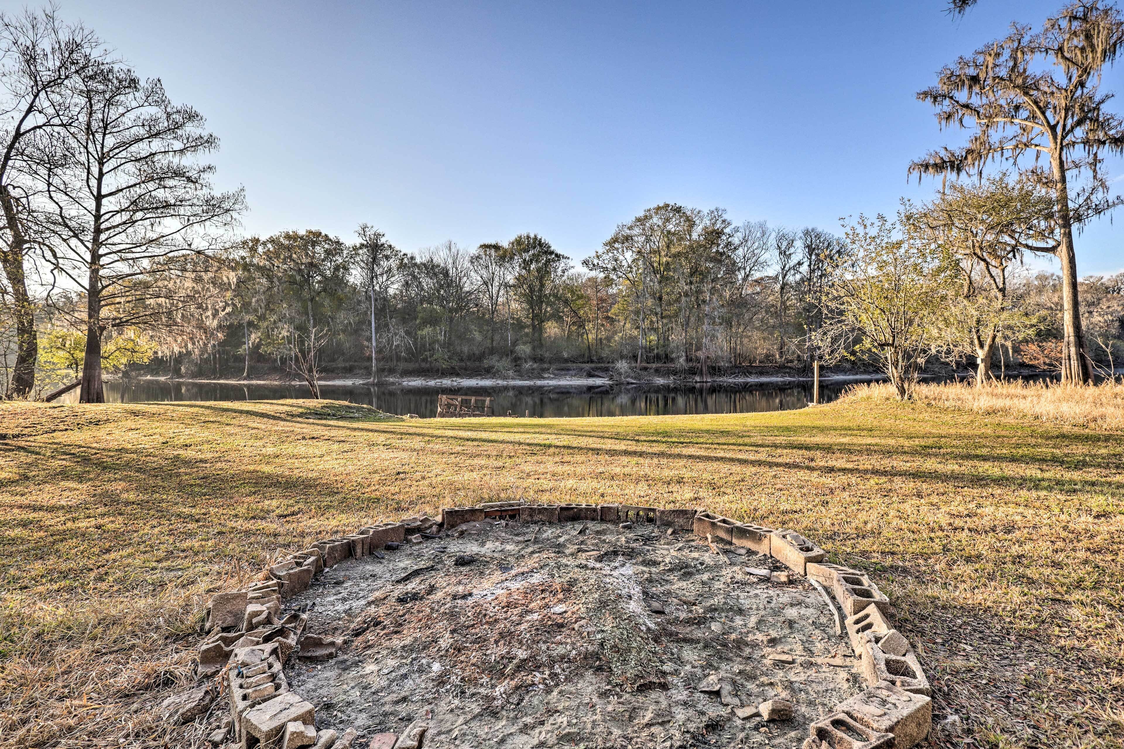 A circular brick fire pit in a grassy field with trees in the background.