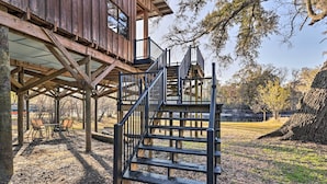 Eine Holzterrasse mit Treppe zu einem überdachten Bereich, umgeben von Bäumen und einer grünen Wiese.
