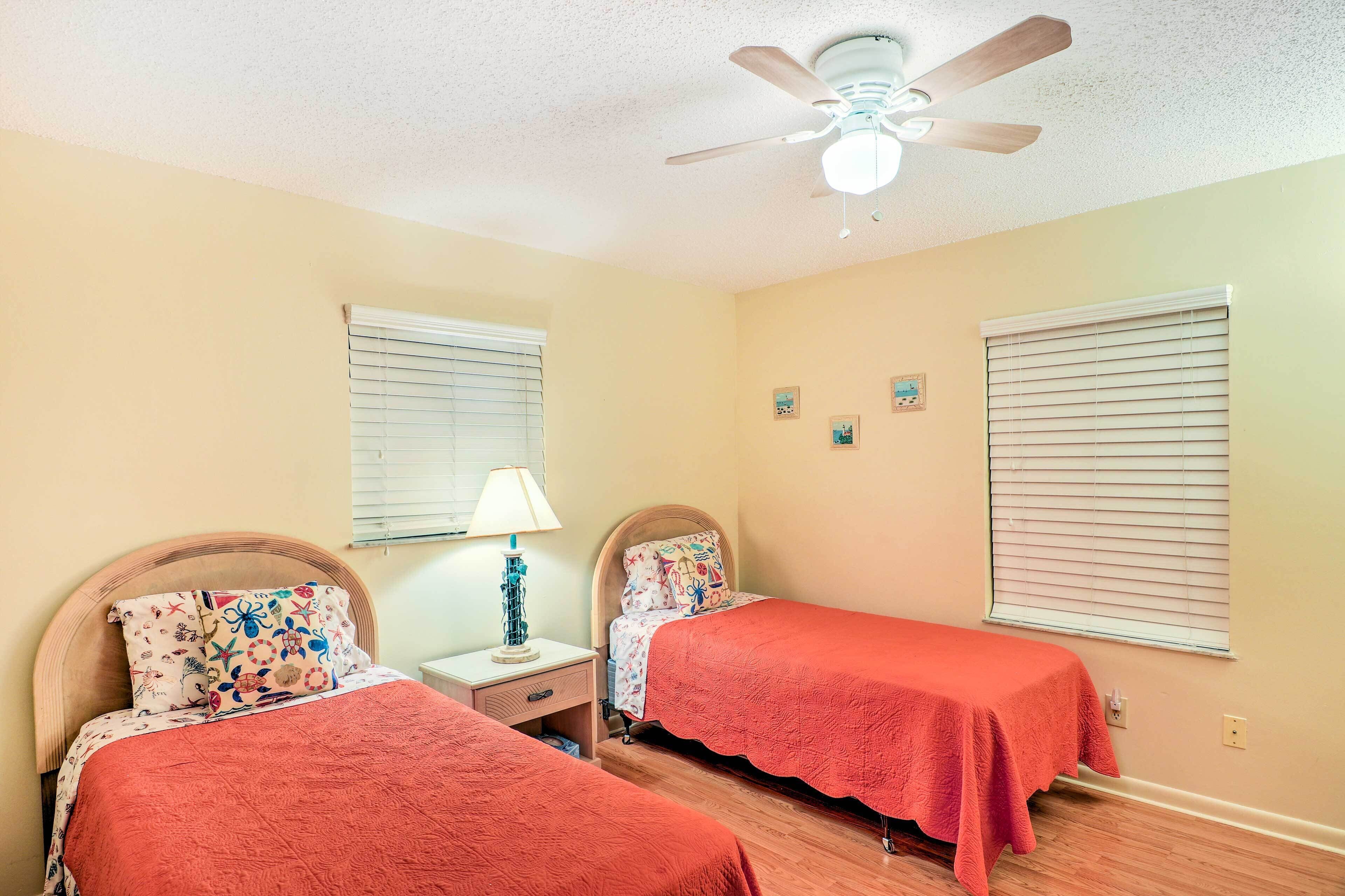 A bedroom with two beds, a ceiling fan, and a nightstand with a lamp.