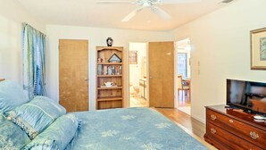 Ein Schlafzimmer mit einem Bett, einem Deckenventilator, einem Bücherregal, einem Fernseher und einer offenen Tür zu einem Badezimmer.
