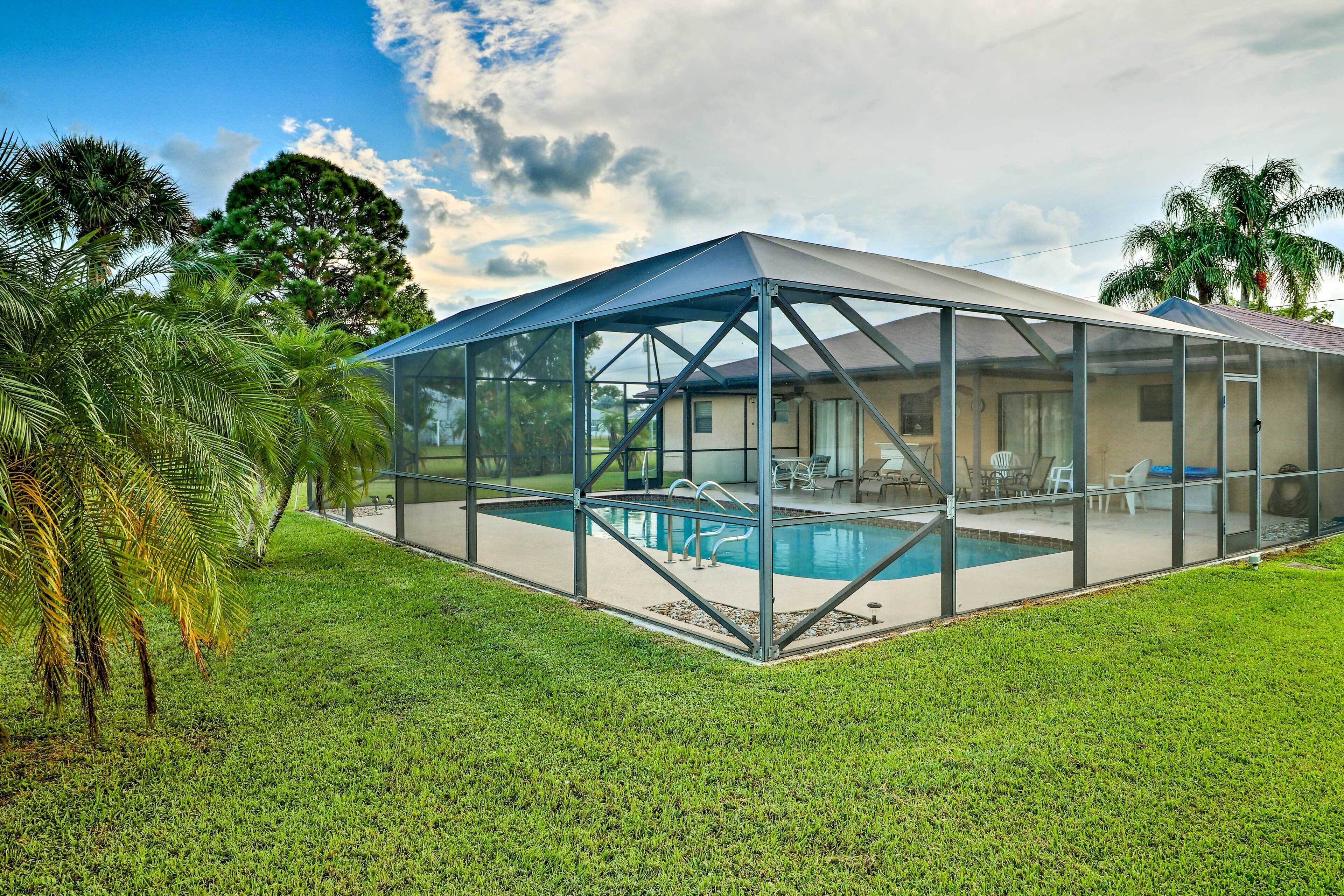A covered swimming pool with a glass enclosure, surrounded by a grassy lawn and palm trees.