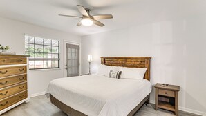Ein Schlafzimmer mit Bett, Holzkommode, Nachttisch, Deckenventilator, Fenster und Lampe.