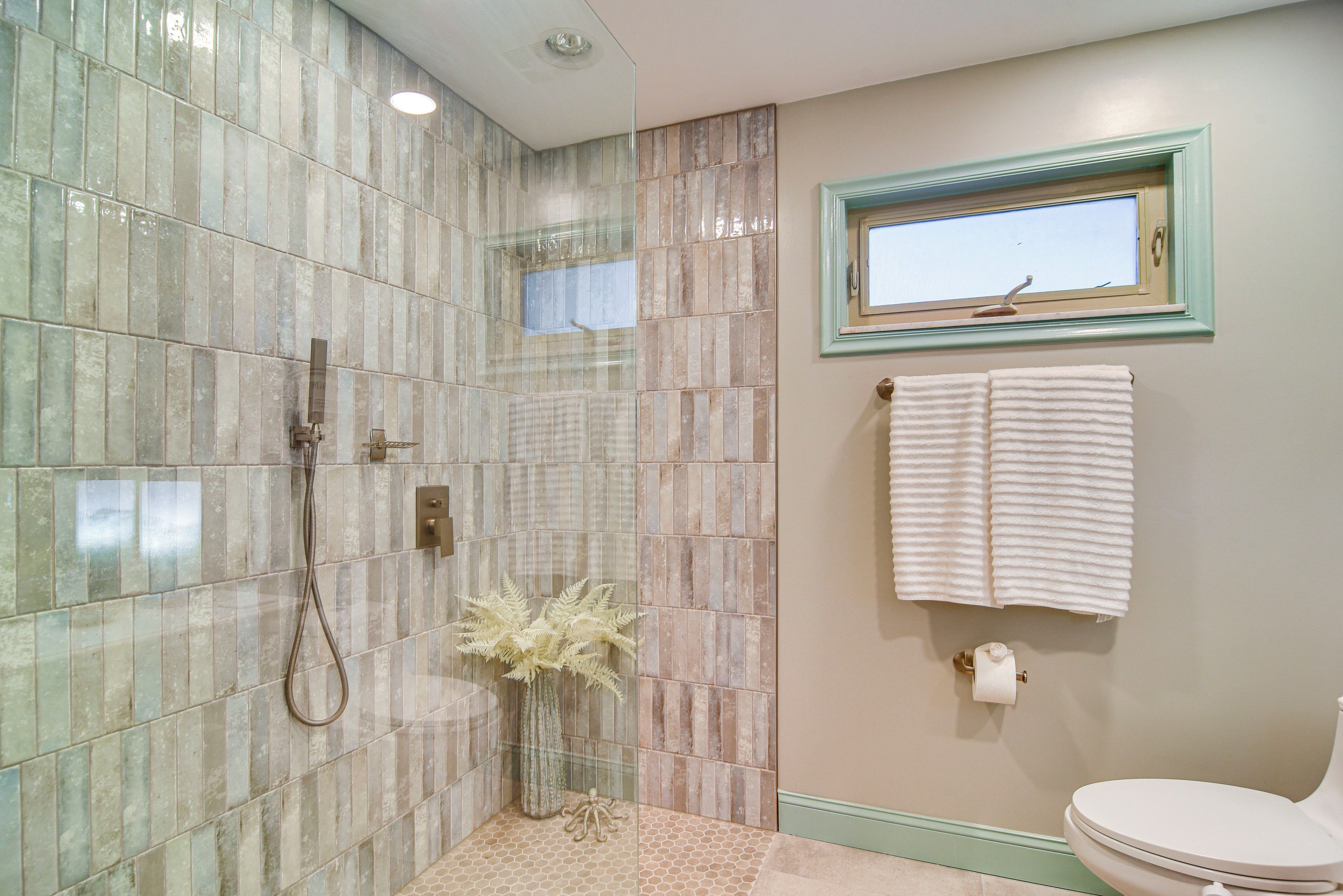 Une salle de bain avec une douche à parois de verre, des toilettes et une fenêtre sur laquelle est accrochée une serviette.