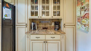 A kitchen with light-colored cabinets, a granite countertop, a coffee maker, and a refrigerator.