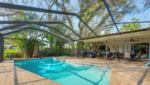 A covered swimming pool with a patio area, lounge chairs, and a view of trees.