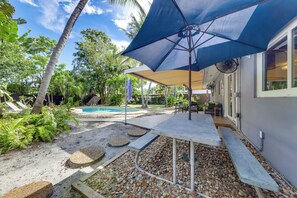 Zona de piscina con un porche cubierto, rodeada de vegetación tropical.