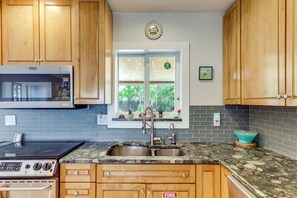 Una cocina con armarios de madera, un lavamanos de acero inoxidable, un microondas y una estufa.
