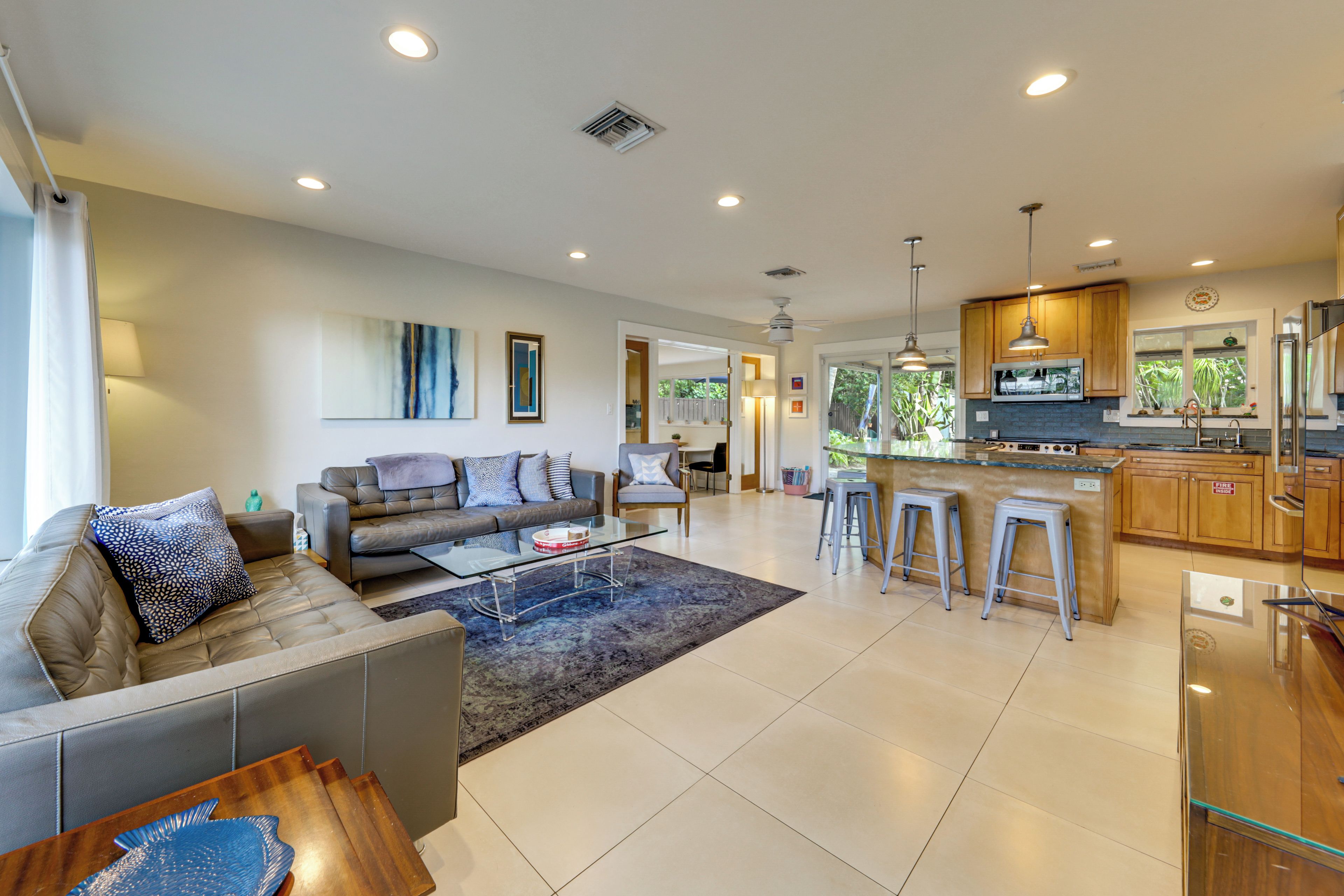 A modern kitchen with a central island, bar stools, and a dining area with a sofa and coffee table.