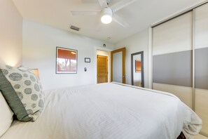 Quarto de hotel com cama, ventilador de teto, quadro emoldurado e porta de correr.