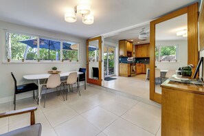 Una cocina moderna con armarios de madera, un comedor con mesa y sillas, y ventanas amplias con parasoles.