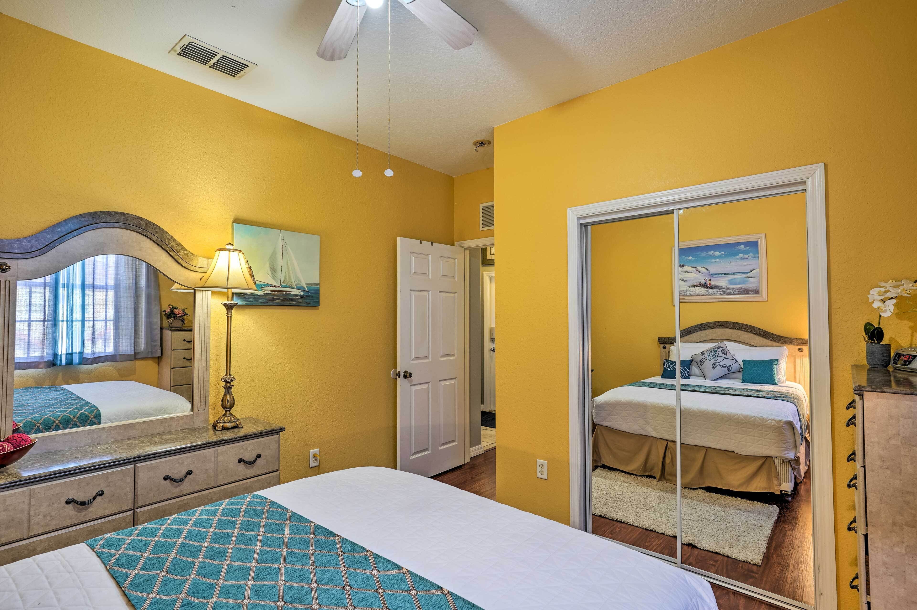 Une chambre à coucher comprenant un lit, une table de chevet, une lampe, une commode, un miroir et une porte donnant sur une autre pièce.