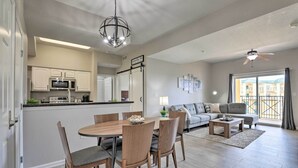 Amplia sala de estar con mesa de comedor, sillas, sofá y mesa de centro. Cuenta con una zona de cocina con microondas y armarios. La habitación tiene ventilador de techo y vistas a un balcón.