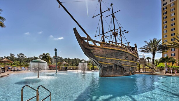 Una piscina con una escultura de barco, sillas de descanso y una fuente.