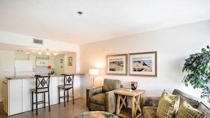 A modern living room with a glass coffee table, a sofa, and a kitchen area in the background. - Resort-style Condo w/ Pool: 19 Miles to Fort Myers (Punta Gorda)