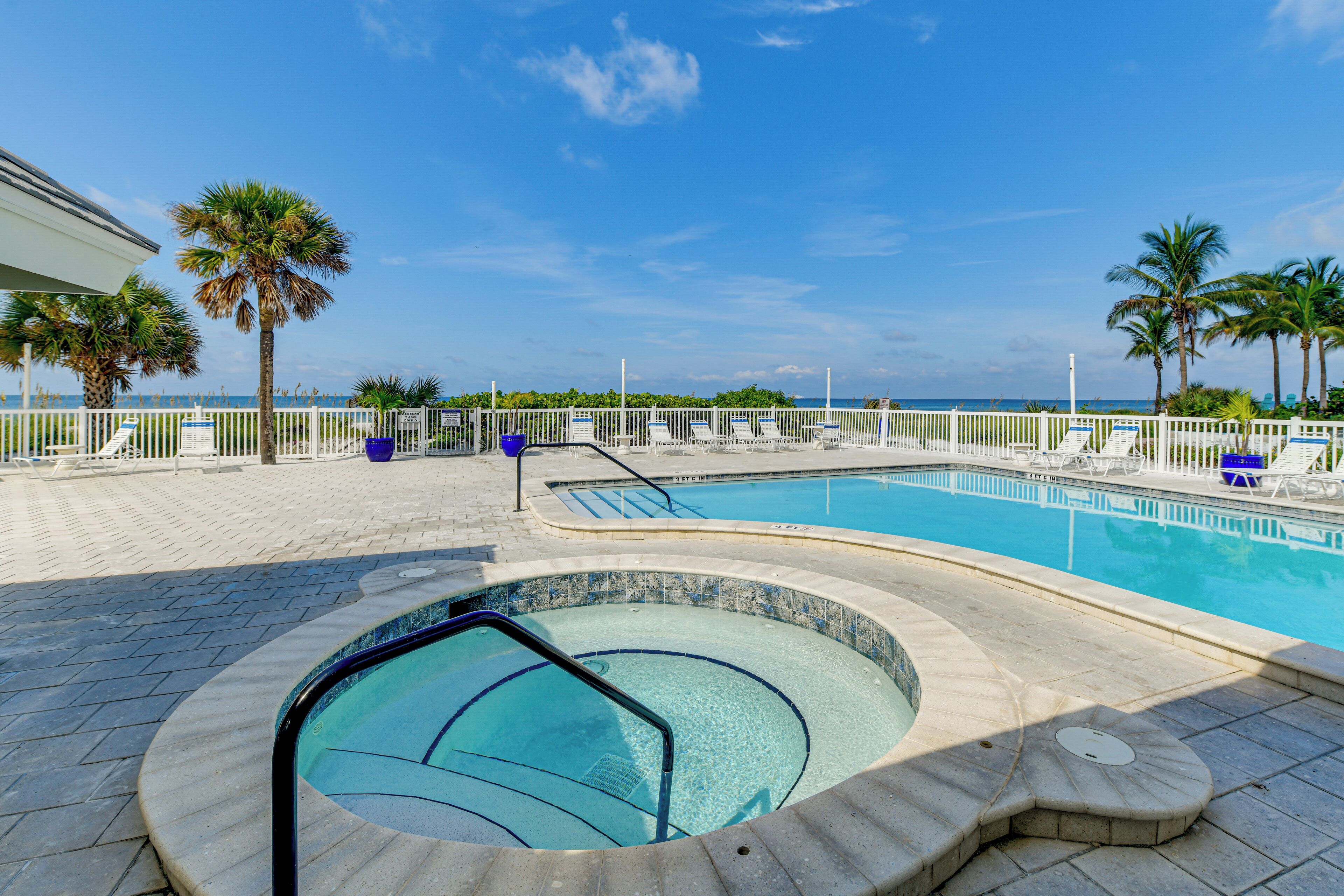 A pool area with a hot tub, lounge chairs, and palm trees.
