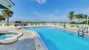 En pool med en djupmarkering som visar 1,8 meters djup, omgiven av solstolar och palmer, med utsikt över havet.