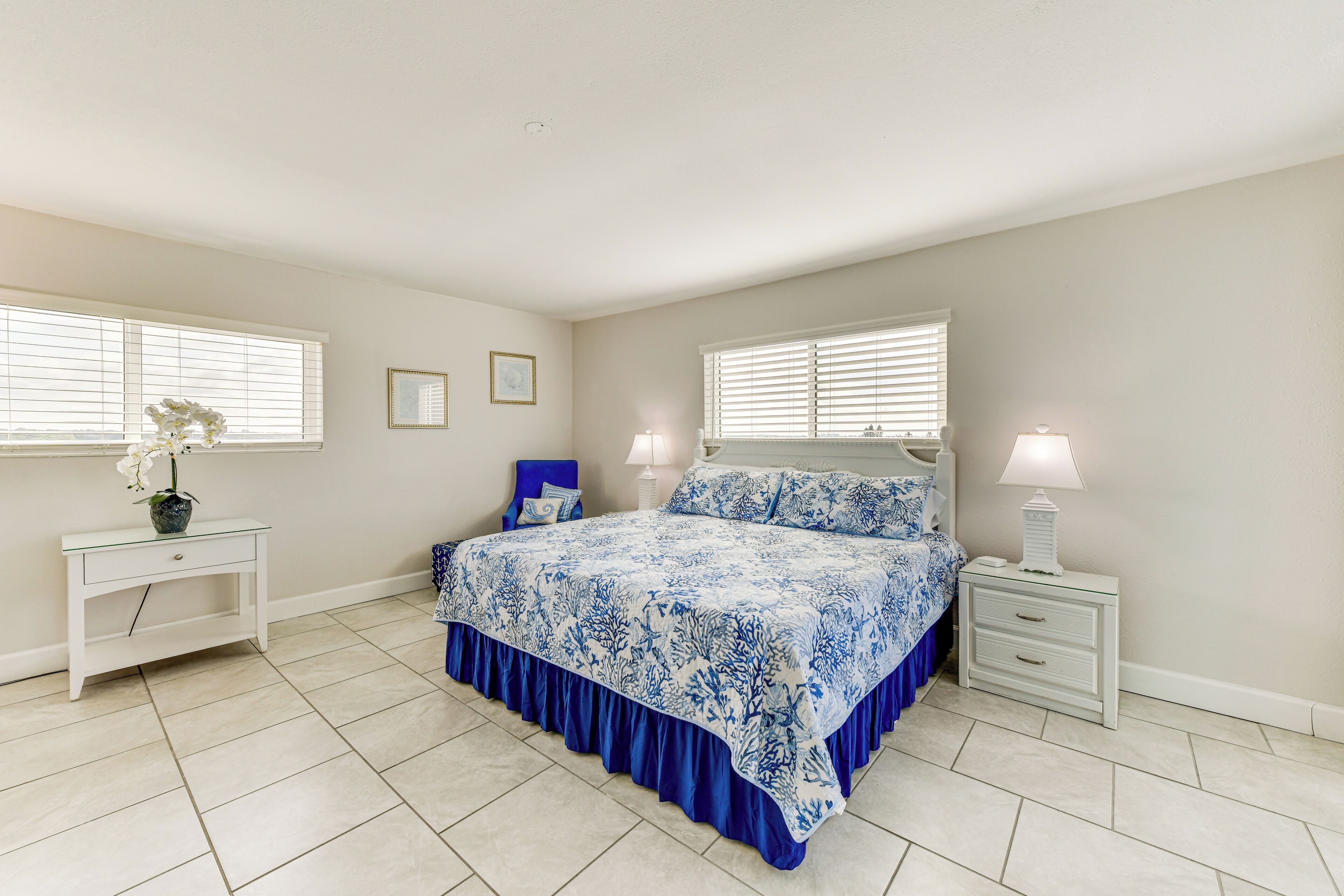 A bedroom with a large bed, two bedside tables, a nightstand, a dresser, and a window with blinds.
