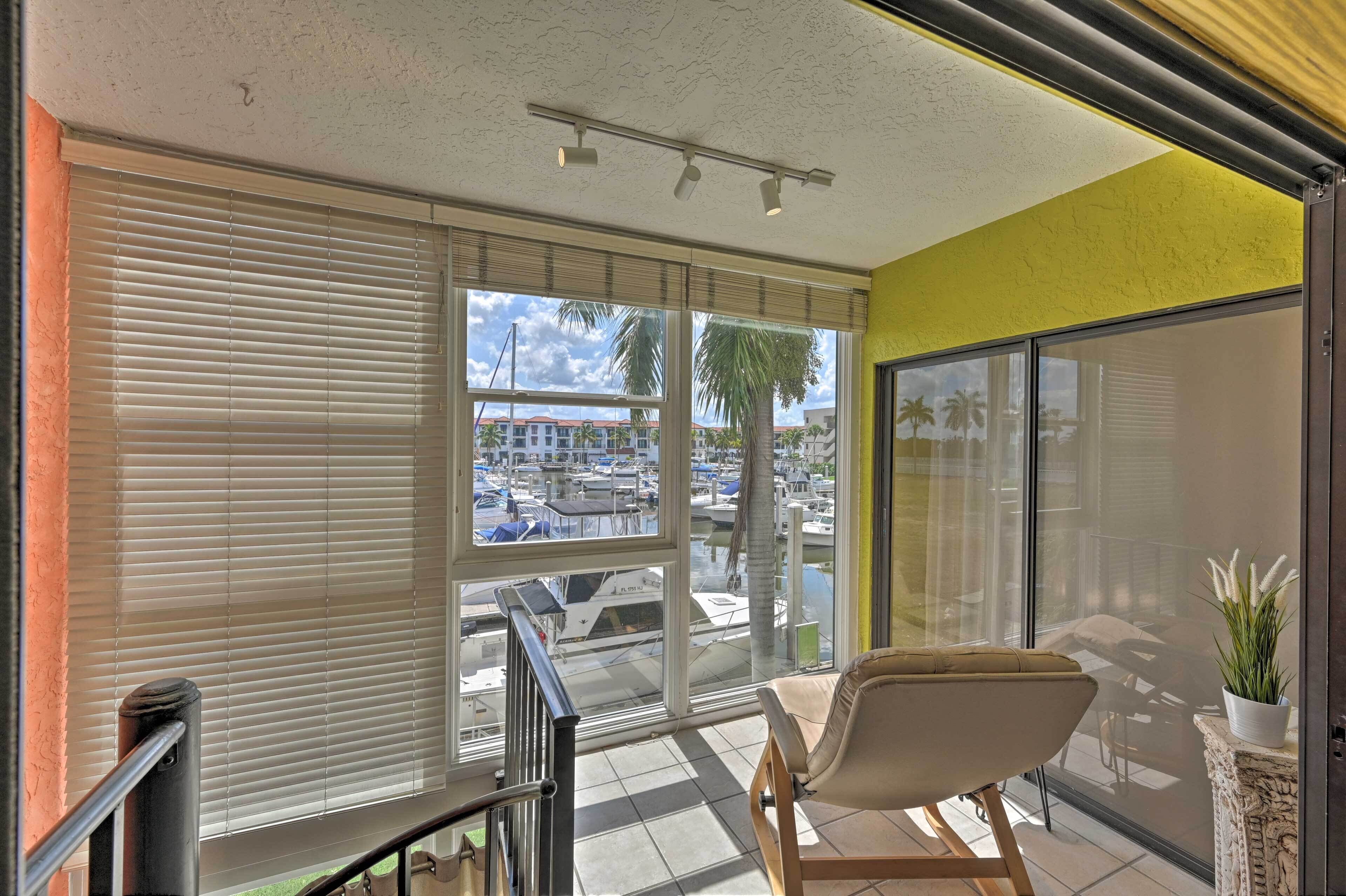 A balcony with a view of boats, a chair, and a potted plant.