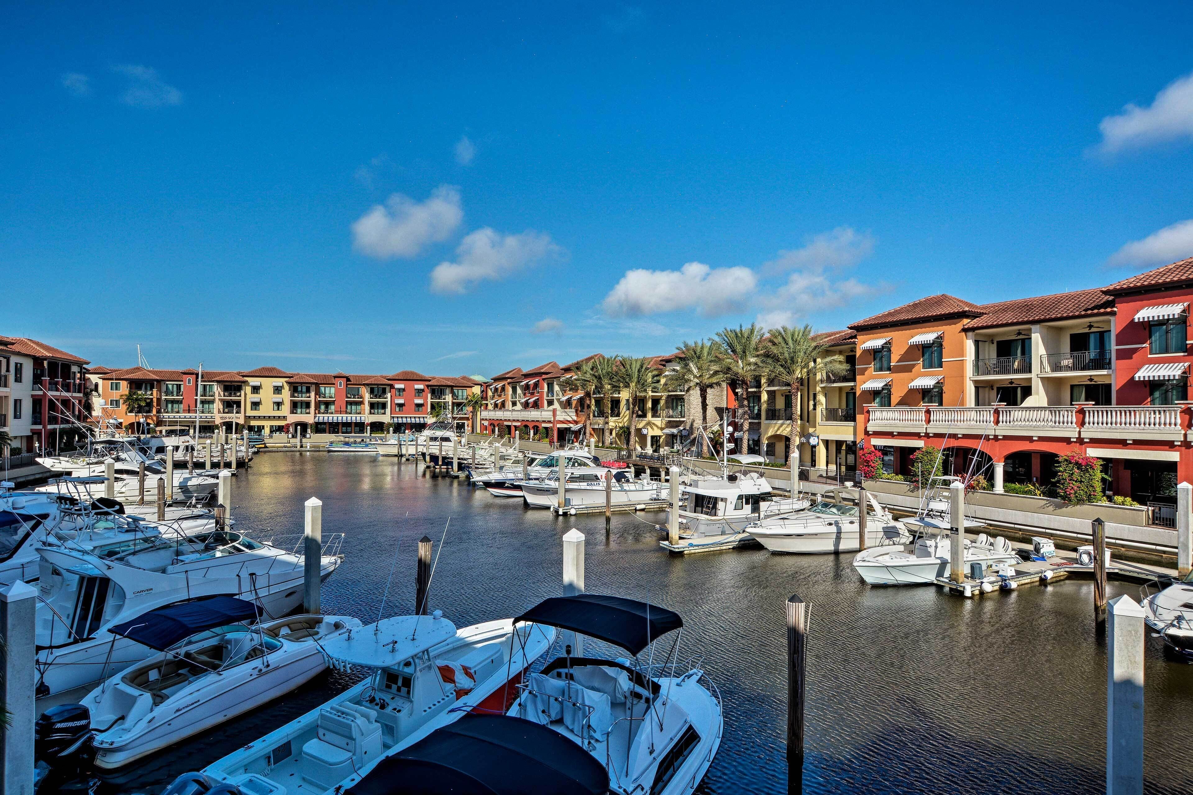 A marina with boats docked, surrounded by multi-story buildings with balconies and palm trees.