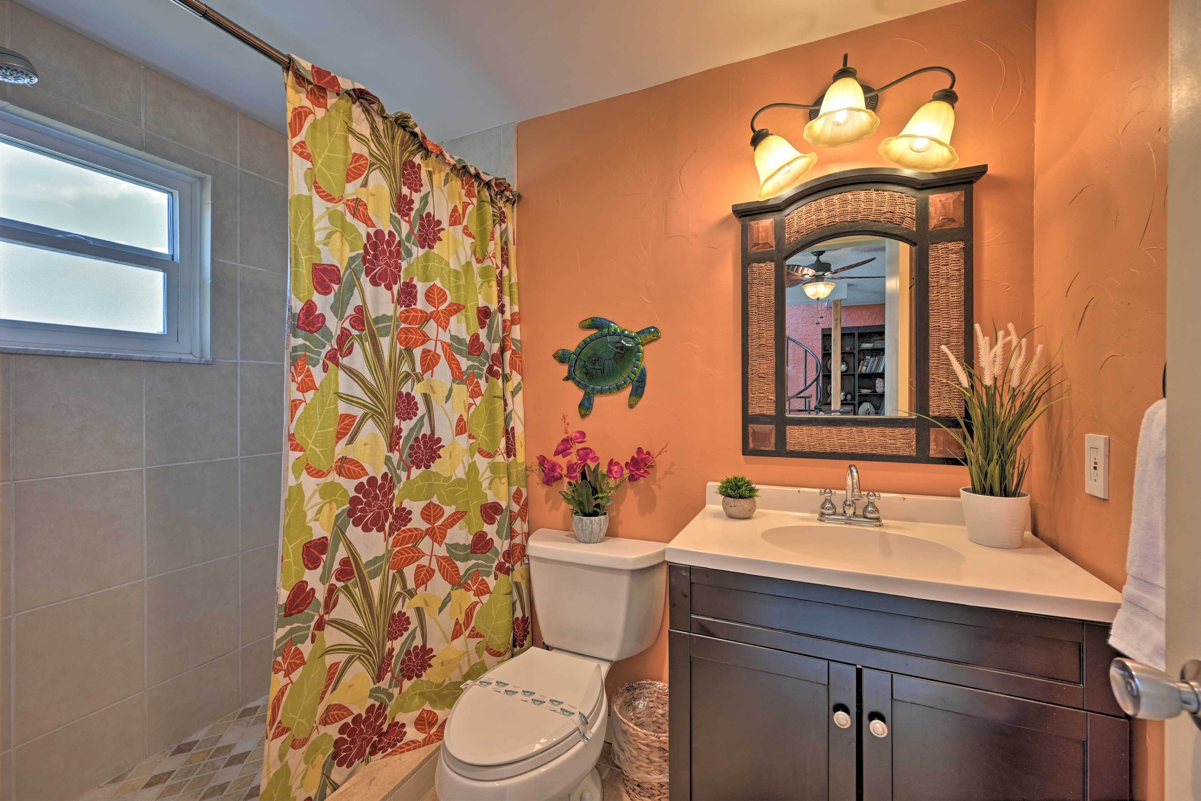 A bathroom with a floral shower curtain, a white toilet, a sink with a mirror above it, and a ceiling fan.