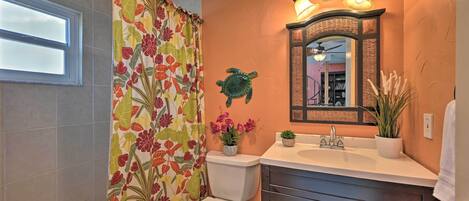 A bathroom with a floral shower curtain, a white toilet, a sink with a mirror above it, and a ceiling fan.