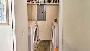 A laundry room with two washing machines, a utility cabinet, and a shelf with various items. - Quincy Home w/ Deck & Outdoor Patio Furniture (Quincy)
