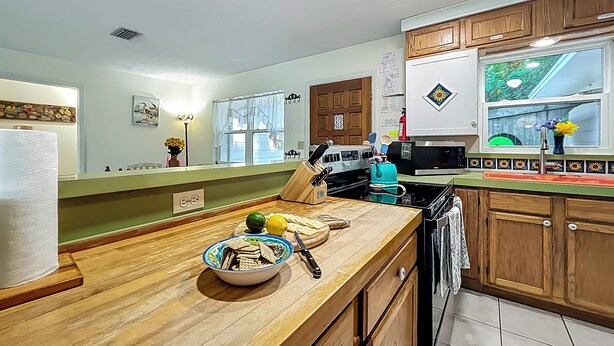 A kitchen with wooden cabinets, a wooden countertop, a sink, and a window with a view of greenery. - Dock & Kayaks: Riverfront Dunnellon Home! (Dunnellon)