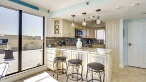 A kitchen with a large island, bar stools, a microwave, and a view of the beach through a sliding door. - Resort-style Penthouse w/ Patio in Hudson! (Hudson)