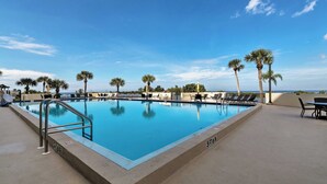 A rectangular pool with a metal ladder on one side, surrounded by lounge chairs and palm trees. - Resort-style Penthouse w/ Patio in Hudson! (Hudson)