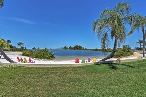 A beach with colorful Adirondack chairs lined up on the sand, a palm tree, and a body of water in the background. - Resort-style Penthouse w/ Patio in Hudson! (Hudson)