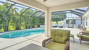 Zona de piscina con un porche acristalado, mobiliario de mimbre y vistas a una piscina y follaje.