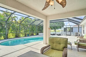 Un espace aménagé au bord de la piscine, doté d’un patio fermé par des baies vitrées, de meubles en osier et offrant une vue sur la piscine et la verdure environnante.
