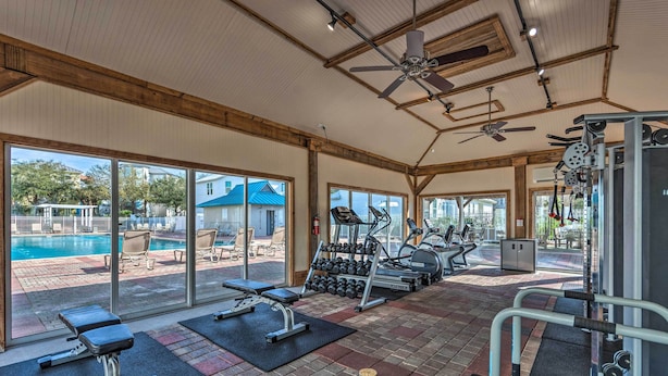 Une salle de sport équipée de matériel d’exercice, d’un banc et offrant une vue sur une piscine et un espace extérieur aménagé pour se détendre.