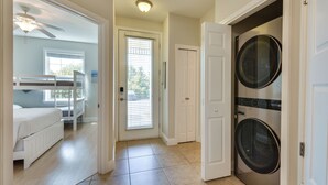 Une buanderie équipée de deux machines à laver, une porte donnant sur une chambre avec un lit superposé et un ventilateur de plafond.