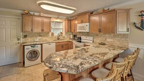 Una cocina con armarios de madera, microondas integrado, lavadora y encimera de mármol.