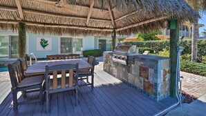Un patio al aire libre con mesa y sillas de madera, una parrilla y techo de paja.