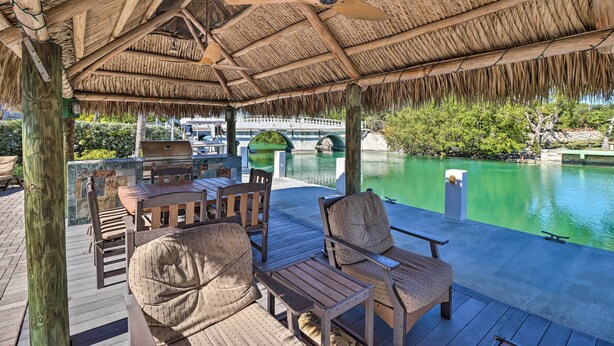 Un patio exterior con mobiliario de madera y techo de paja, con vistas a una piscina.